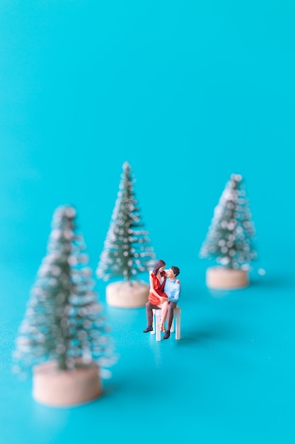 Gente en miniatura, pareja de enamorados sentados junto a un árbol de Navidad, concepto de Navidad y feliz año nuevo.