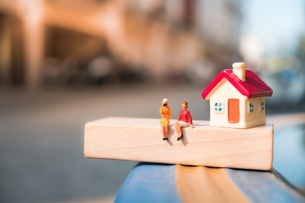Gente miniatura, pareja mujer sentada en el número de bloque de madera con mini casa utilizando como negocio, soc