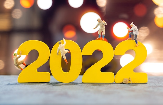 Gente en miniatura subiendo en madera con el número 2022, feliz año nuevo concepto