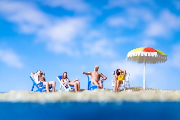 Gente en miniatura tomando el sol en el baech con cielo azul, concepto de horario de verano