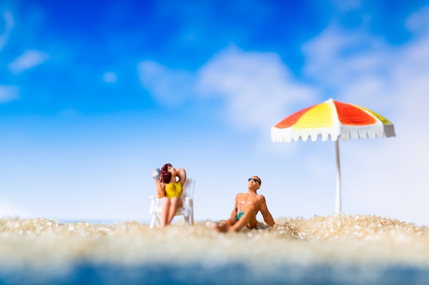 Gente miniatura tomando el sol en la playa, el concepto de horario de verano