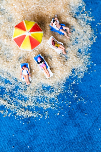 Gente miniatura tomando el sol en la playa, el concepto de horario de verano