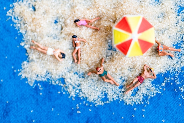 Gente miniatura tomando el sol en la playa, el concepto de horario de verano