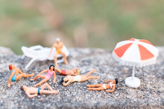 Gente en miniatura vistiendo traje de baño tomando el sol en una roca