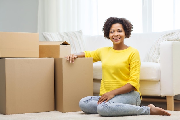 gente, mudanza de nuevo lugar y concepto de reparación - feliz joven afroamericana con muchas cajas de cartón sentadas en el suelo en casa