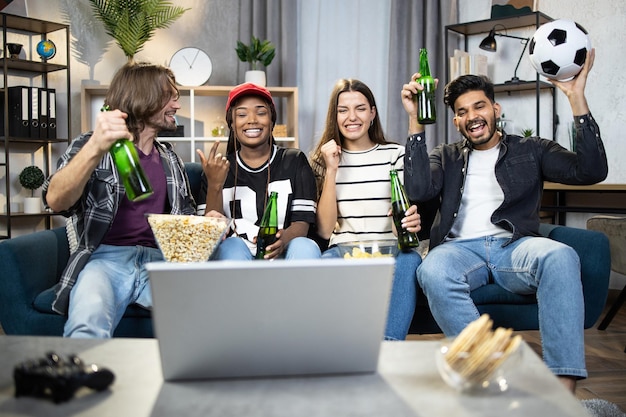 Gente multirracial viendo un partido de fútbol en una laptop en casa