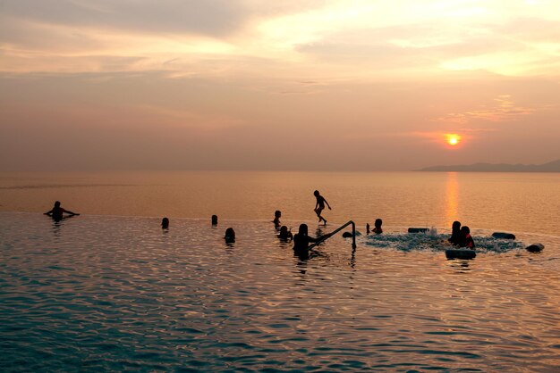 Gente nadando divirtiéndose en la piscina - Jóvenes disfrutando de vacaciones en un hotel tropical y hermosa puesta de sol en el mar a la hora del crepúsculo - Filtro Vintage