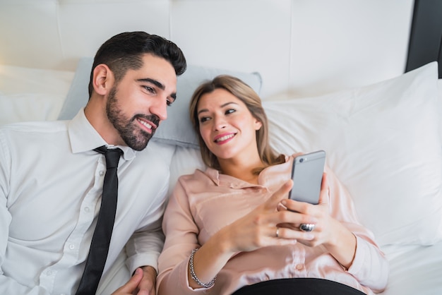 Gente de negocios acostada en la cama y mediante teléfono móvil.