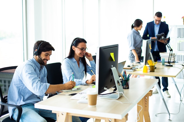 Gente de negocios atractiva en auriculares sonríe mientras trabaja con la computadora en la oficina moderna