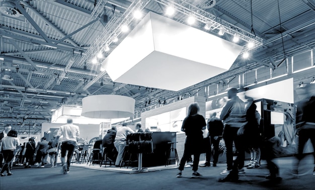 Gente de negocios caminando entre stands de ferias comerciales en una sala de exposiciones de eventos públicos