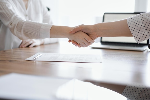 Gente de negocios dándose la mano por encima de los papeles del contrato recién firmados en la mesa de madera, de cerca. Abogados en la reunión. Trabajo en equipo, asociación, concepto de éxito.