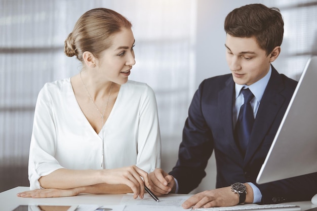 Gente de negocios discutiendo algo mientras está sentada en una oficina soleada. Concéntrese en la mujer de negocios mientras habla con su colega masculino.