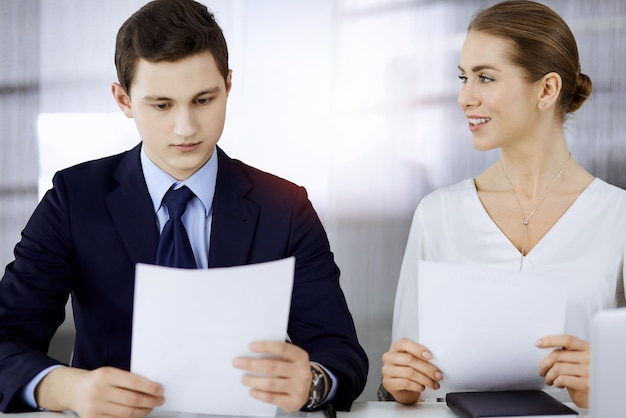 Gente de negocios discutiendo algo mientras está sentada en una oficina soleada. Concéntrese en la mujer de negocios mientras habla con su colega masculino.