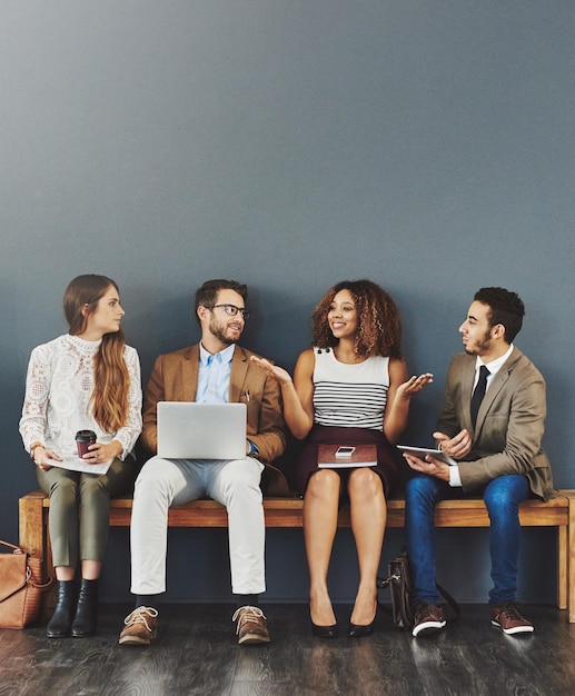 Gente de negocios feliz trabajando con tecnología hablando mientras está sentada en una fila contra un fondo gris Equipo de marketing digital joven colaborando en redes en línea para anunciar una startup