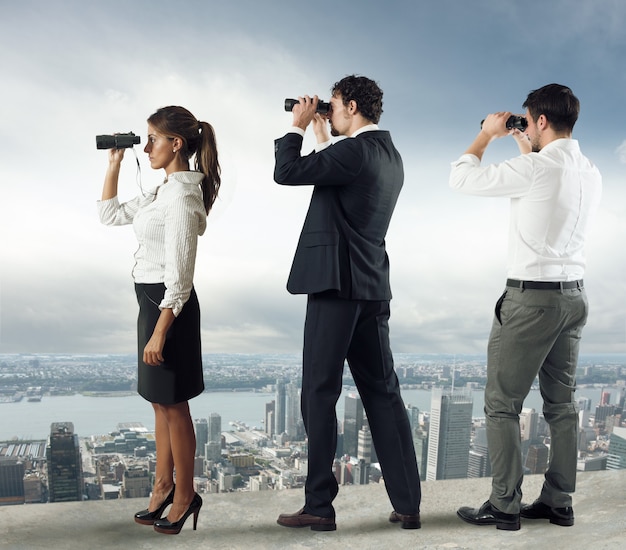 La gente de negocios mira la ciudad desde el techo con binoculares.