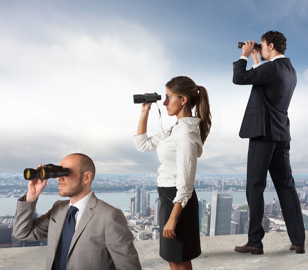 La gente de negocios mira la ciudad desde el techo con binoculares.