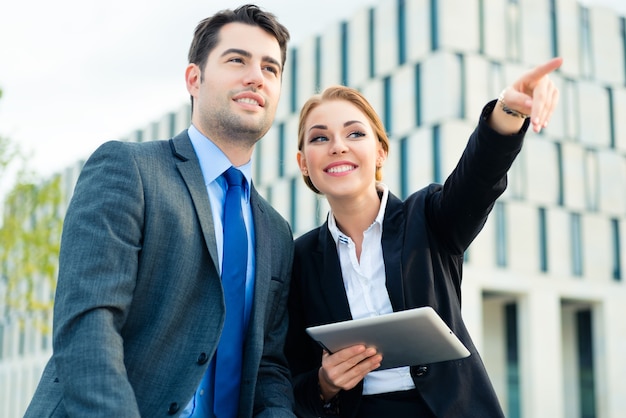 Gente de negocios o empresario y empresaria que trabajan al aire libre, con almohadilla o tableta