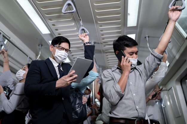 Gente de negocios de pie en el metro de tránsito masivo. Hombre usando tableta y teléfono inteligente. personas que usan mascarilla. Virus de la gripe coronavirus en los viajes públicos.