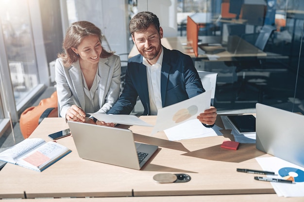 Gente de negocios positiva en la computadora portátil durante una reunión que discute gráficos financieros