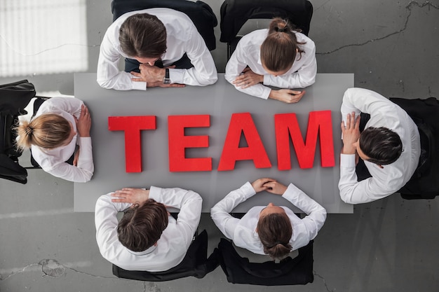 Foto gente de negocios sentada alrededor de la mesa con letras rojas equipo, concepto de trabajo en equipo de trabajo en equipo