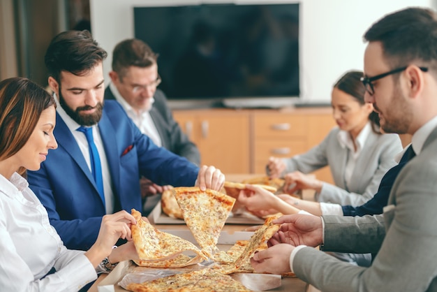 Gente de negocios sentado en la sala de juntas y almorzando pizza.