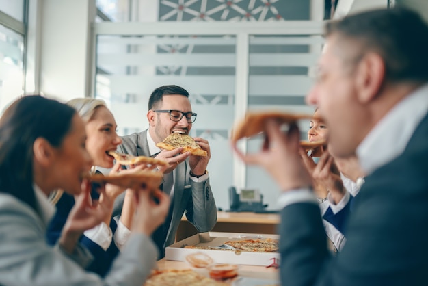 Gente de negocios sentado en la sala de juntas y almorzando pizza.