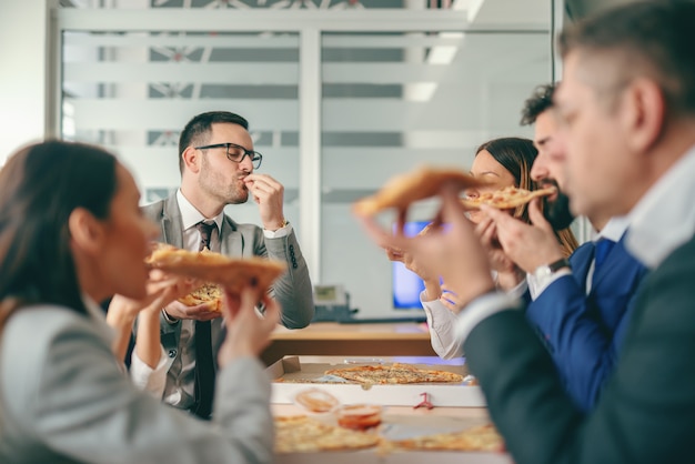 Gente de negocios sentado en la sala de juntas y almorzando pizza.