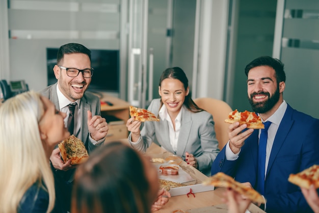 Gente de negocios sentado en la sala de juntas y almorzando pizza.