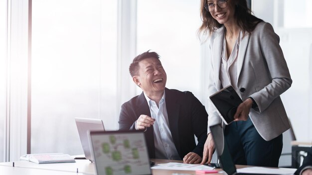 Foto gente de negocios sonriente en la sala de reuniones discute el proyecto usando una computadora portátil y una tableta