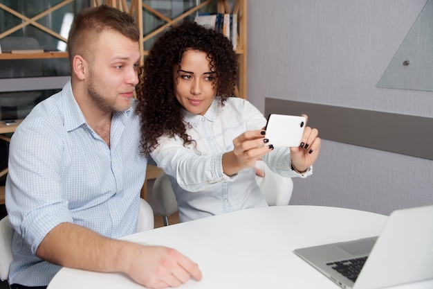 Gente de negocios sonriente tomando selfie en smartphone mientras está sentado en el escritorio en la oficina