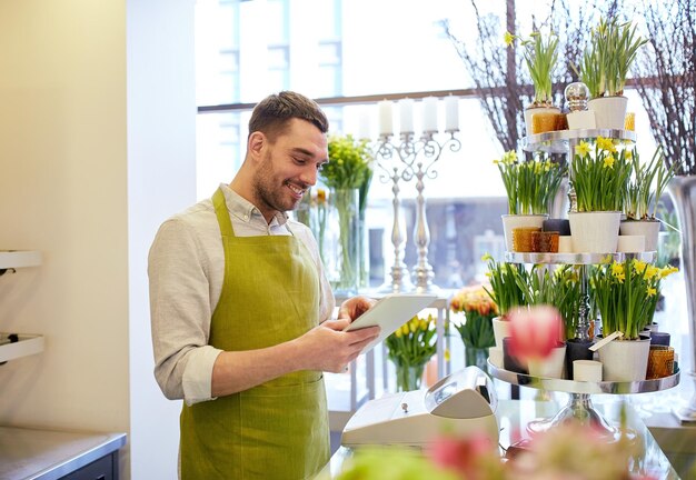 gente, negocios, tecnología, venta y floristería y concepto - florista sonriente feliz con computadora de tablet pc en el mostrador de la floristería