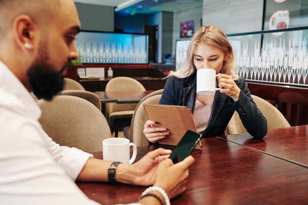 Gente de negocios tomando café y leyendo noticias y artículos en la tableta y el teléfono inteligente en la cafetería de la oficina