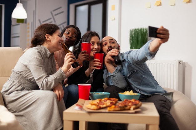 Gente de negocios tomando fotos en el teléfono inteligente en la fiesta de la oficina con bebidas y bocadillos después de las horas de trabajo. Colegas que usan teléfonos móviles para tomar selfies y crear recuerdos en una celebración divertida.