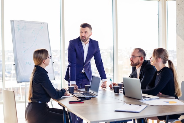 Gente de negocios trabajando juntos en una oficina moderna con vistas al paisaje urbano. El director le informa al personal sobre las nuevas tecnologías. Concepto de trabajo de oficina