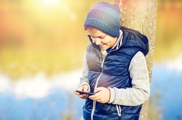 la gente, los niños y el concepto de tecnología - un adolescente feliz jugando o enviando mensajes de texto en el teléfono inteligente al aire libre