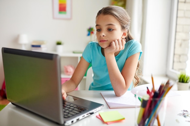 Gente, niños, educación y concepto de aprendizaje: chica aburrida con computadora portátil y cuaderno haciendo la tarea en casa