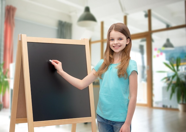 gente, niños, publicidad y concepto de educación - niña feliz con pizarra y tiza sobre el fondo de la sala de clase de la escuela