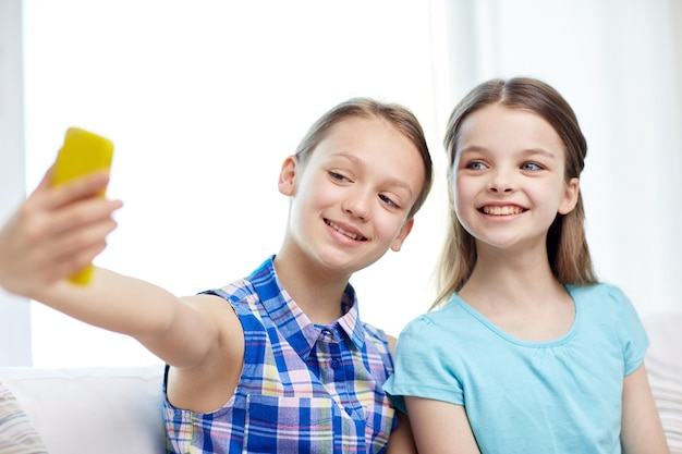 gente, niños, tecnología, amigos y concepto de amistad - niñas felices sentadas en el sofá y tomándose selfie con un smartphone en casa