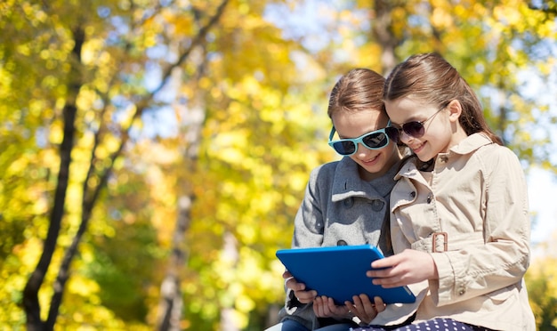 gente, niños, tecnología, temporada y concepto de amistad - niñas felices con gafas de sol con computadora de tablet pc sobre el fondo del parque de otoño