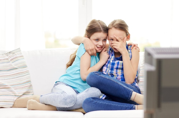gente, niños, televisión, amigos y concepto de amistad - dos niñas asustadas viendo horror en la televisión en casa