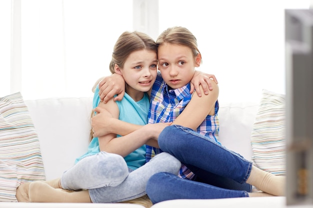 gente, niños, televisión, amigos y concepto de amistad - dos niñas asustadas viendo horror en la televisión en casa