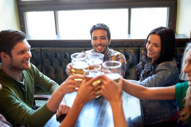 gente, ocio, amistad y concepto de celebración - amigos felices bebiendo cerveza de barril y vasos tintineantes en el bar o pub