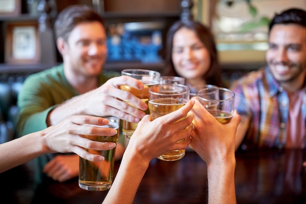 Foto gente, ocio, amistad y concepto de celebración - amigos felices bebiendo cerveza de barril y vasos tintineantes en el bar o pub