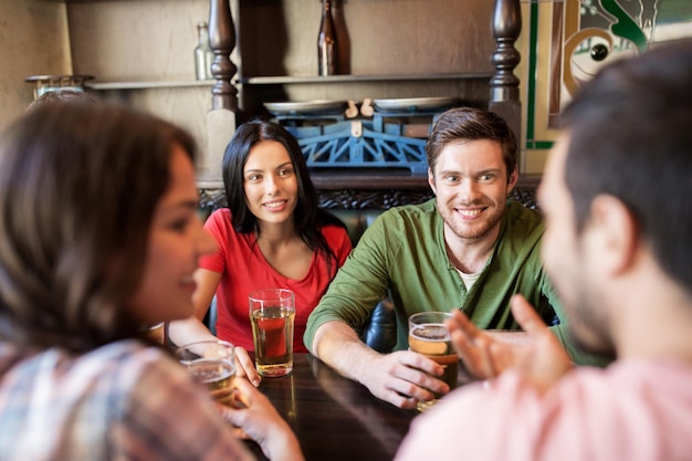 gente, ocio, amistad y concepto de comunicación - amigos felices bebiendo cerveza y hablando en el bar o pub