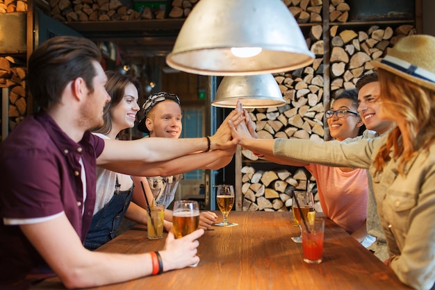 Foto gente, ocio, amistad y concepto de comunicación - grupo de amigos sonrientes felices con bebidas haciendo gestos de cinco en el bar o pub