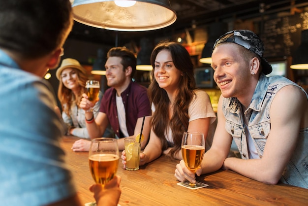 gente, ocio, amistad y concepto de comunicación - grupo de amigos sonrientes felices bebiendo cerveza y cócteles hablando en el bar o pub