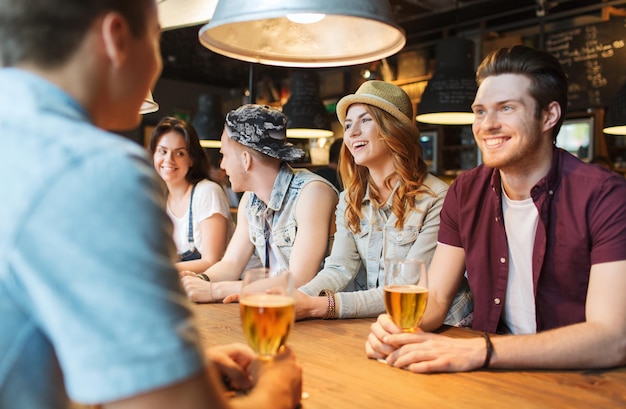gente, ocio, amistad y concepto de comunicación - grupo de amigos sonrientes felices bebiendo cerveza y hablando en el bar o pub