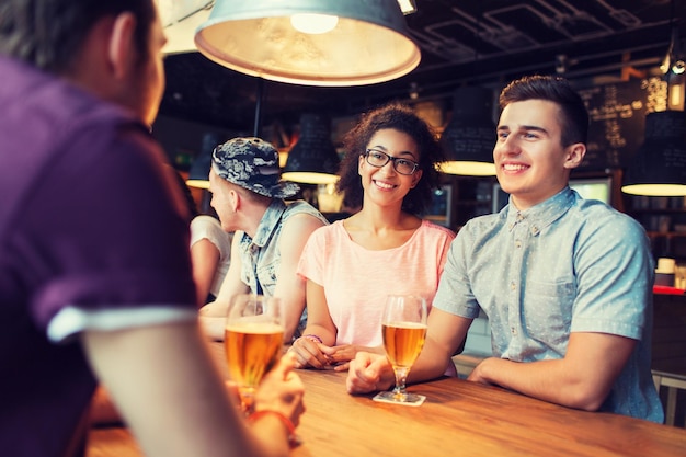 Foto gente, ocio, amistad y concepto de comunicación - grupo de amigos sonrientes felices bebiendo cerveza y hablando en el bar o pub