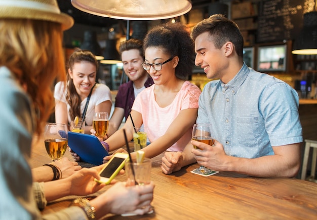 gente, ocio, amistad y concepto de comunicación - grupo de amigos sonrientes felices con tablet pc y bebidas en el bar o pub