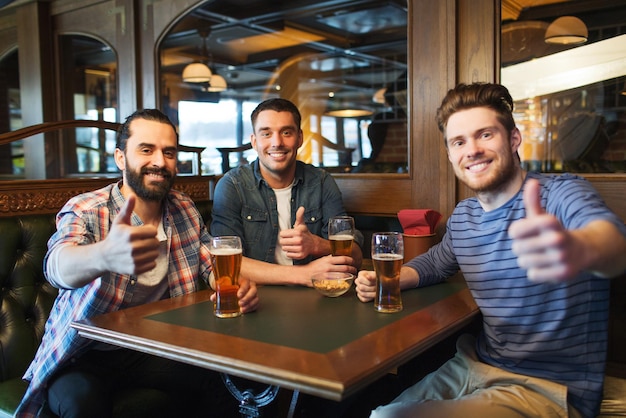 gente, ocio, amistad y concepto de despedida de soltero - amigos varones felices bebiendo cerveza y mostrando los pulgares hacia arriba en el bar o pub